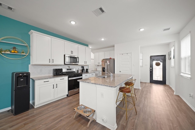 5958 First Blush Dr, Katy, TX 77493 - kitchen with stainless steel appliances, dark wood finished floors, tasteful backsplash, white cabinets, and a kitchen island with sink