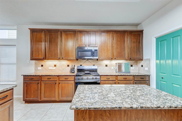 2961 Autumn Brook Ln, League City, TX 77573 - kitchen featuring appliances with stainless steel finishes, light stone countertops, brown cabinets, tasteful backsplash, and light tile patterned floors