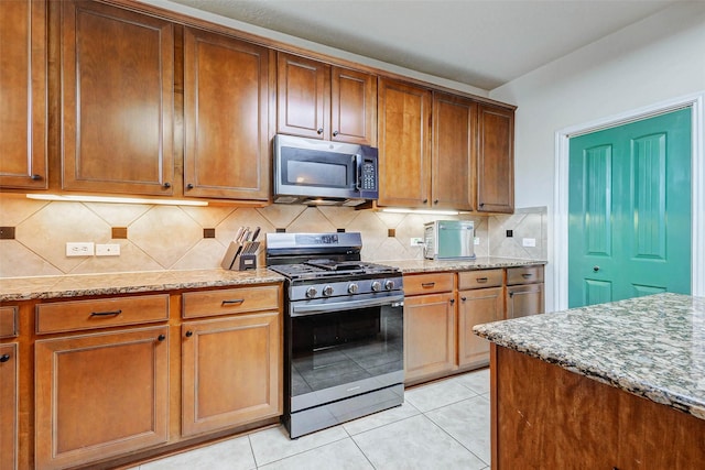 2961 Autumn Brook Ln, League City, TX 77573 - kitchen with stainless steel appliances, light stone counters, tasteful backsplash, light tile patterned floors, and brown cabinetry