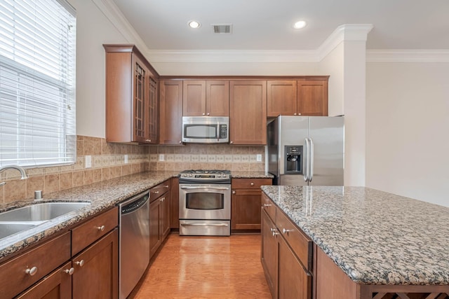 5817 Katy St, Houston, TX 77007 - kitchen featuring stainless steel appliances, brown cabinetry, light stone counters, glass insert cabinets, and crown molding
