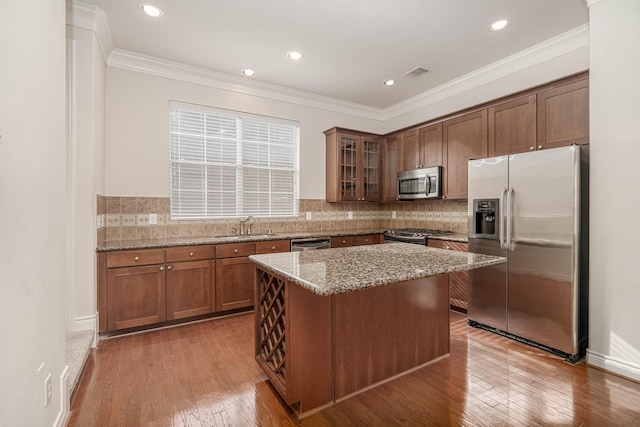5817 Katy St, Houston, TX 77007 - kitchen featuring stainless steel appliances, light stone counters, hardwood / wood-style floors, glass insert cabinets, and ornamental molding