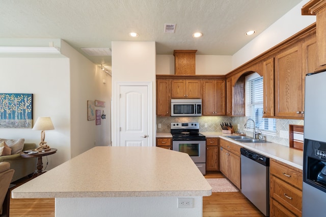 129 Lakeshore Dr, Onalaska, TX 77360 - kitchen featuring appliances with stainless steel finishes, light wood-style flooring, a kitchen island, decorative backsplash, and light countertops