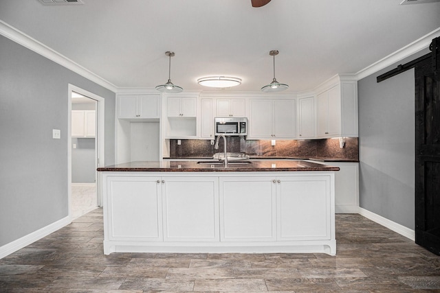3014 Bayou Dr, La Porte, TX 77571 - kitchen with stainless steel microwave, white cabinetry, tasteful backsplash, dark stone countertops, and ornamental molding