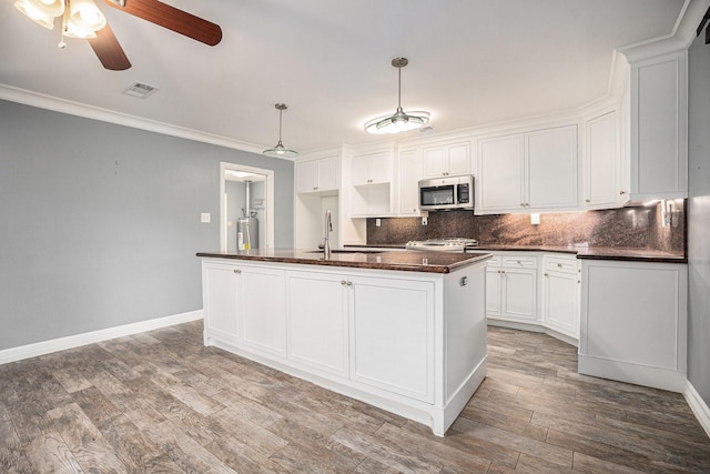 3014 Bayou Dr, La Porte, TX 77571 - kitchen with stainless steel microwave, dark countertops, a ceiling fan, decorative backsplash, and white cabinetry