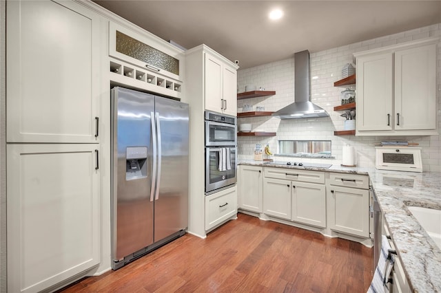 10252 Sunset Ln, Conroe, TX 77385 - kitchen featuring appliances with stainless steel finishes, open shelves, wall chimney exhaust hood, decorative backsplash, and wood finished floors