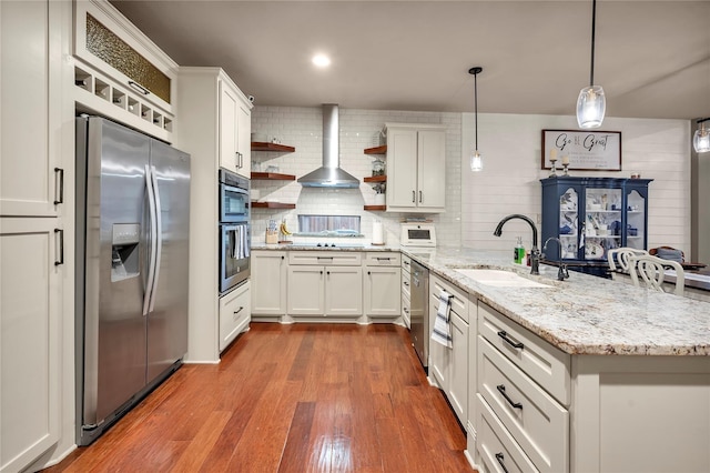 10252 Sunset Ln, Conroe, TX 77385 - kitchen with stainless steel appliances, wall chimney exhaust hood, a peninsula, open shelves, and wood finished floors