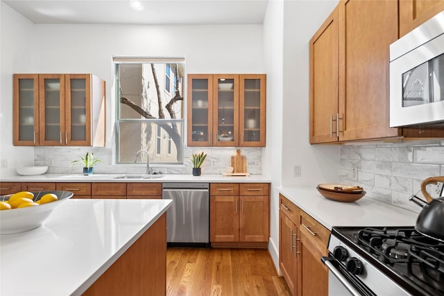 2310 Arabelle St, Houston, TX 77007 - kitchen featuring appliances with stainless steel finishes, brown cabinets, decorative backsplash, light wood finished floors, and light countertops