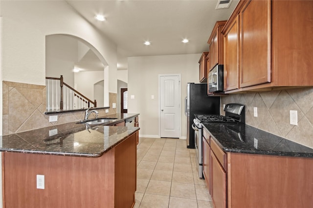 187 Black Swan Pl, The Woodlands, TX 77354 - kitchen with stainless steel appliances, brown cabinetry, arched walkways, light tile patterned flooring, and tasteful backsplash