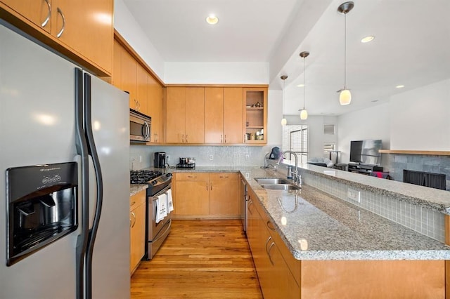 4707 Caroline St, Houston, TX 77004 - kitchen featuring appliances with stainless steel finishes, a peninsula, light wood finished floors, backsplash, and a tiled fireplace