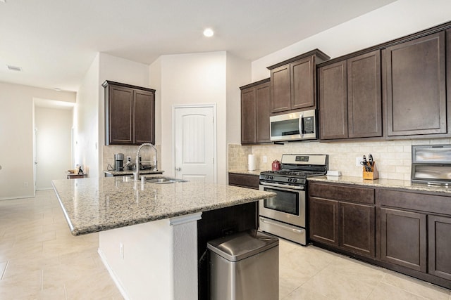 23719 Scotsman Dr, Katy, TX 77493 - kitchen featuring appliances with stainless steel finishes, backsplash, light stone countertops, dark brown cabinets, and an island with sink
