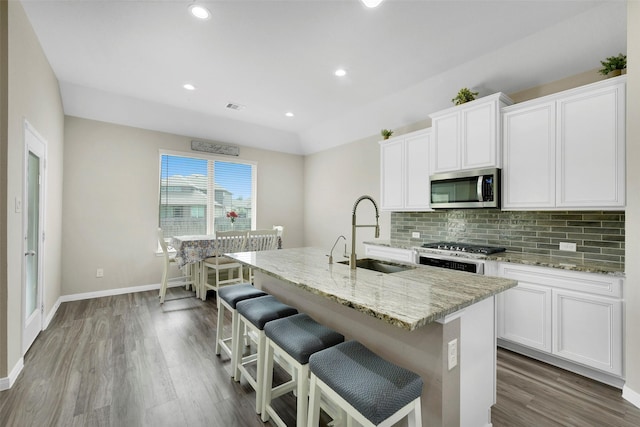 12806 Durham Creek Ln, Tomball, TX 77375 - kitchen featuring stainless steel microwave, dark wood-type flooring, an island with sink, backsplash, and light stone counters
