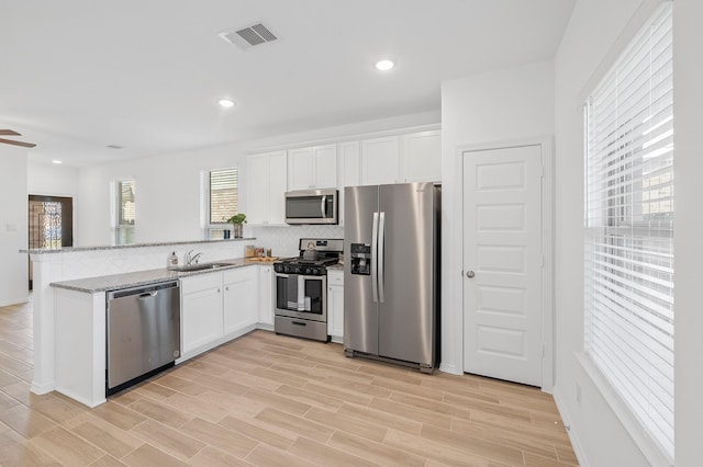 5630 Tabula Rasa Dr, Katy, TX 77493 - kitchen featuring appliances with stainless steel finishes, a peninsula, white cabinetry, light stone counters, and recessed lighting