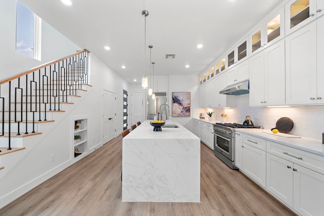 408 E 33rd St, Houston, TX 77018 - kitchen with stainless steel appliances, under cabinet range hood, light wood-style flooring, a center island with sink, and tasteful backsplash