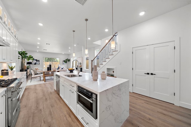 408 E 33rd St, Houston, TX 77018 - kitchen featuring appliances with stainless steel finishes, light wood-style flooring, white cabinetry, an island with sink, and glass insert cabinets