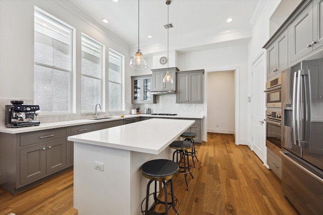 1240 W 16th St, Houston, TX 77008 - kitchen with gray cabinetry, appliances with stainless steel finishes, a breakfast bar area, ornamental molding, and a kitchen island