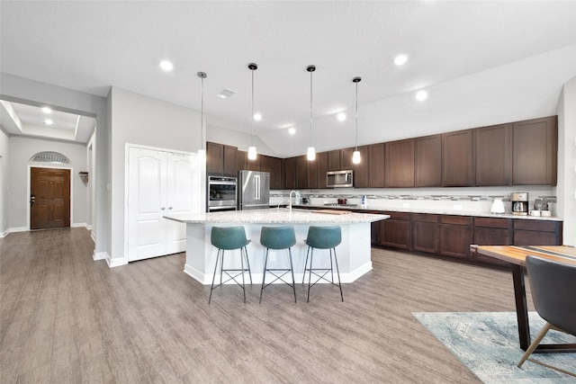 15715 Holloway Creek Ct, Houston, TX 77044 - kitchen with appliances with stainless steel finishes, dark brown cabinets, a center island with sink, light wood-style floors, and recessed lighting