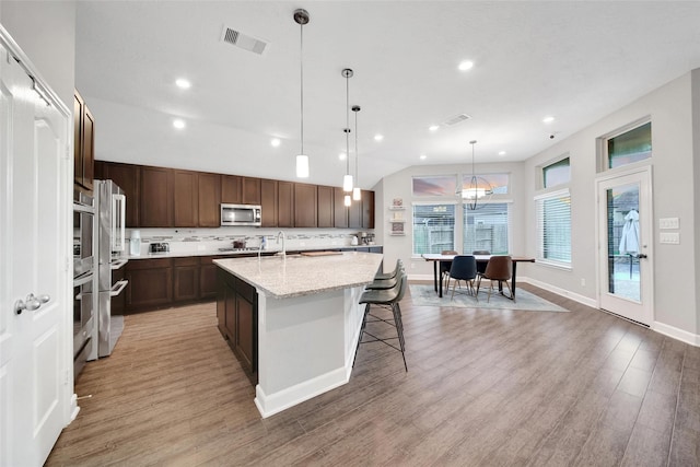 15715 Holloway Creek Ct, Houston, TX 77044 - kitchen with stainless steel microwave, light wood-style floors, a center island with sink, backsplash, and dark brown cabinets