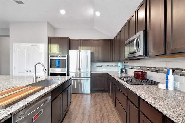15715 Holloway Creek Ct, Houston, TX 77044 - kitchen featuring appliances with stainless steel finishes, dark brown cabinets, light wood-style floors, tasteful backsplash, and lofted ceiling