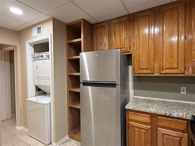 2213 S Braeswood Blvd Unit 13C, Houston, TX 77030 - kitchen with freestanding refrigerator, stacked washer and clothes dryer, brown cabinetry, light tile patterned floors, and a drop ceiling