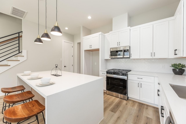 3310 Bremond St, Houston, TX 77004 - kitchen with appliances with stainless steel finishes, a breakfast bar, light wood-style floors, backsplash, and white cabinets