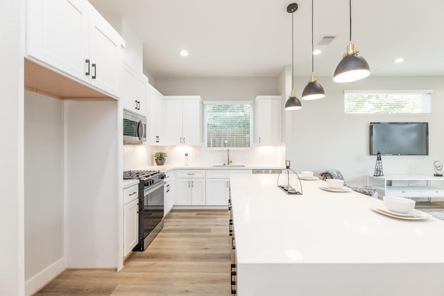 3310 Bremond St, Houston, TX 77004 - kitchen with stainless steel appliances, white cabinetry, light wood finished floors, a kitchen island, and light countertops