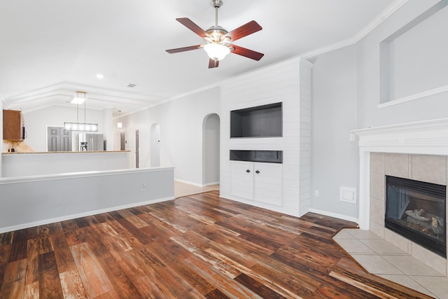 17919 Eagle Pass Falls Ct, Humble, TX 77346 - unfurnished living room featuring a tiled fireplace, a ceiling fan, dark wood-type flooring, ornamental molding, and vaulted ceiling