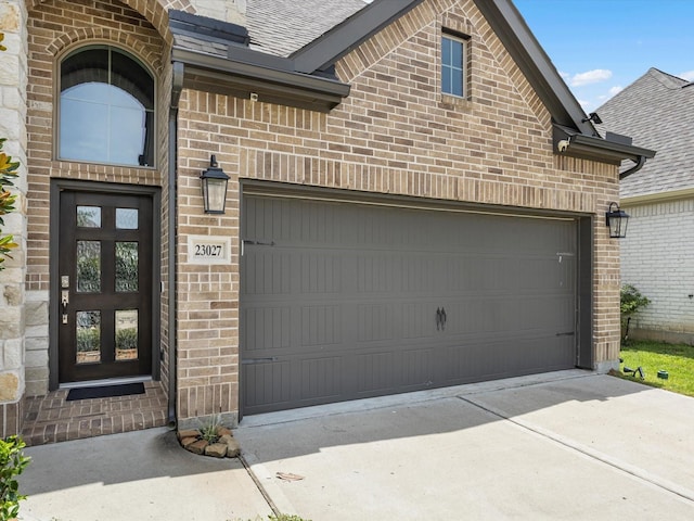 23027 Needlegrass Rd, Katy, TX 77493 - view of exterior entry with brick siding, driveway, roof with shingles, and a garage