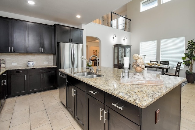 4615 Montcliff Bend Ln, Sugar Land, TX 77479 - kitchen with arched walkways, a center island with sink, light tile patterned floors, appliances with stainless steel finishes, and backsplash