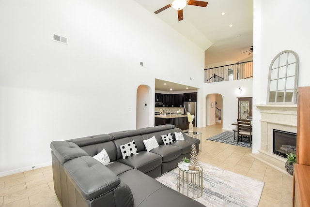 4615 Montcliff Bend Ln, Sugar Land, TX 77479 - living room with arched walkways, a ceiling fan, a high ceiling, light tile patterned flooring, and a glass covered fireplace