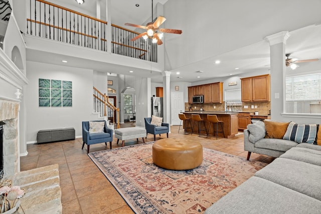 14402 Hazeldale Dr, Cypress, TX 77429 - living area featuring ceiling fan, a tiled fireplace, a towering ceiling, stairway, and healthy amount of natural light