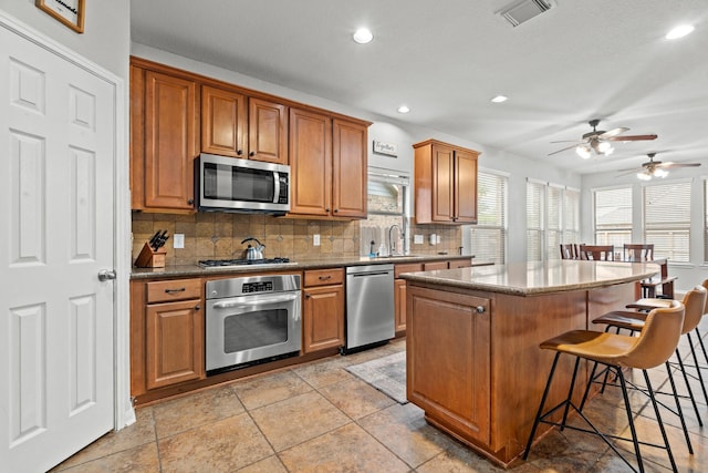14402 Hazeldale Dr, Cypress, TX 77429 - kitchen with stainless steel appliances, a breakfast bar area, decorative backsplash, ceiling fan, and brown cabinetry