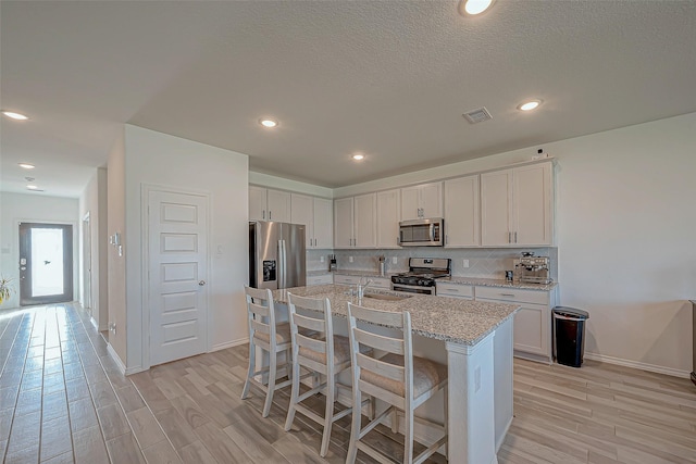 5703 Morning Vista Rd, Katy, TX 77493 - kitchen featuring appliances with stainless steel finishes, light wood-type flooring, an island with sink, white cabinetry, and recessed lighting