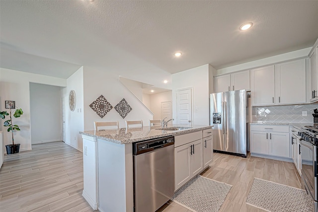 5703 Morning Vista Rd, Katy, TX 77493 - kitchen with stainless steel appliances, light stone countertops, tasteful backsplash, light wood-type flooring, and a center island with sink