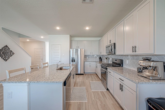 5703 Morning Vista Rd, Katy, TX 77493 - kitchen featuring stainless steel appliances, light wood-style flooring, white cabinetry, an island with sink, and tasteful backsplash