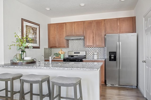 21115 Montego Bay Dr, Cypress, TX 77433 - kitchen with stainless steel appliances, under cabinet range hood, a peninsula, brown cabinets, and tasteful backsplash