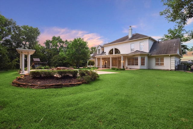 106 Melody Ln, Friendswood, TX 77546 - back of house at dusk featuring a lawn, a chimney, a shingled roof, and stucco siding