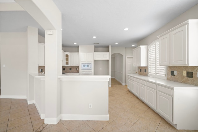 16426 Torry View Ter, Houston, TX 77095 - kitchen featuring white microwave, arched walkways, light tile patterned floors, backsplash, and white cabinets