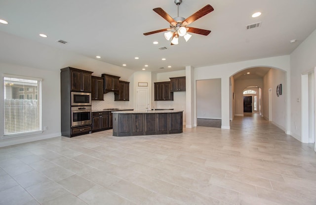 3605 Dolan Trail Ct, Pearland, TX 77584 - kitchen featuring stainless steel appliances, arched walkways, a ceiling fan, dark brown cabinetry, and decorative backsplash