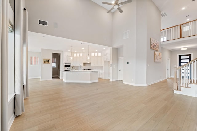 14315 Summer Prairie Trl, Cypress, TX 77433 - unfurnished living room with ceiling fan, a towering ceiling, stairway, and light wood-type flooring