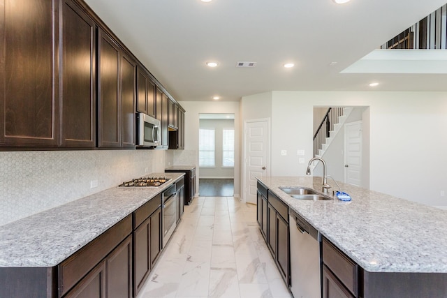 8506 Belfast Manor Ln, Richmond, TX 77407 - kitchen featuring appliances with stainless steel finishes, dark brown cabinetry, a center island with sink, light marble finish floors, and recessed lighting