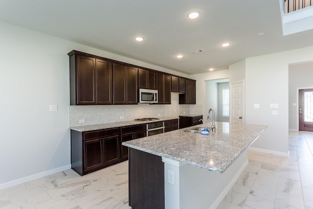 8506 Belfast Manor Ln, Richmond, TX 77407 - kitchen with stainless steel appliances, light marble finish floors, dark brown cabinetry, an island with sink, and backsplash