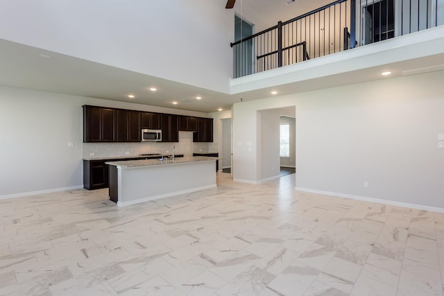 8506 Belfast Manor Ln, Richmond, TX 77407 - kitchen featuring stainless steel microwave, open floor plan, an island with sink, a high ceiling, and dark brown cabinets