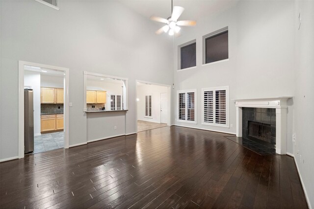 8014 Sports Haven Dr, Humble, TX 77346 - unfurnished living room featuring ceiling fan, a towering ceiling, a tiled fireplace, and dark wood-style flooring