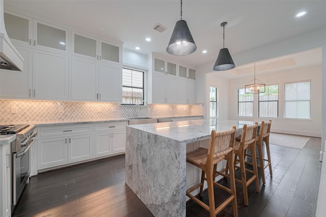 6525 Wharton St, Houston, TX 77055 - kitchen with high end stainless steel range oven, wall chimney range hood, light stone countertops, white cabinetry, and dark wood-style floors