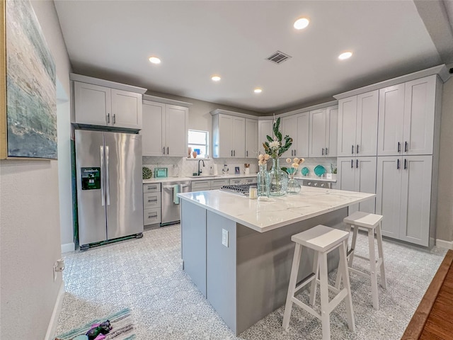 3128 Avenue N, Galveston, TX 77550 - kitchen featuring appliances with stainless steel finishes, tasteful backsplash, a kitchen bar, a kitchen island, and light stone counters