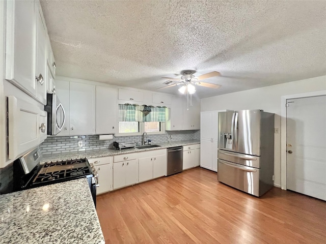 8009 Dellanera Dr, Hitchcock, TX 77563 - kitchen with stainless steel appliances, ceiling fan, light wood-style floors, backsplash, and white cabinets