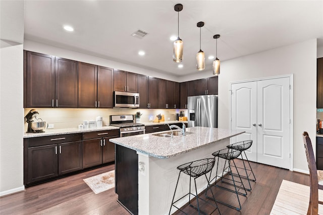 1942 Elkington Cir, Conroe, TX 77304 - kitchen with stainless steel appliances, dark brown cabinetry, dark wood finished floors, a breakfast bar area, and light stone counters