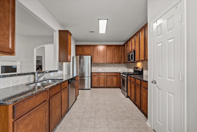 621 Rocky Hollow Ln, League City, TX 77573 - kitchen with appliances with stainless steel finishes, tasteful backsplash, dark stone countertops, arched walkways, and brown cabinetry