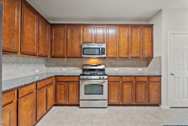 621 Rocky Hollow Ln, League City, TX 77573 - kitchen featuring stainless steel appliances, dark stone countertops, backsplash, brown cabinets, and light tile patterned flooring