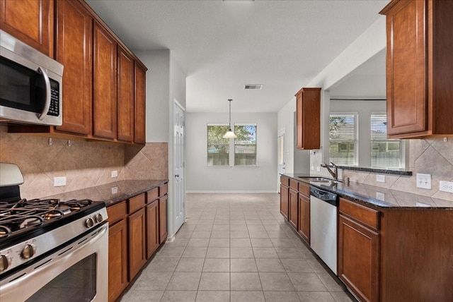 621 Rocky Hollow Ln, League City, TX 77573 - kitchen with stainless steel appliances, dark stone counters, backsplash, brown cabinetry, and light tile patterned floors